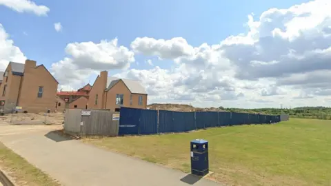 Google Large open grass area separated from houses under construction by a blue fence