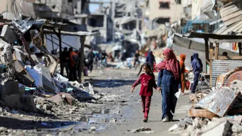 Reuters Palestinians walk past destroyed buildings in Gaza City (20 March 2024)