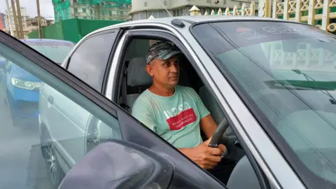 Jayantha Athukorala sits in his car with the door open