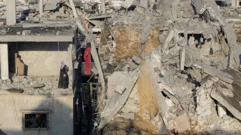 Reuters A Palestinian woman stands in a destroyed room of a building following Israeli air strikes in Khan Younis, in the south of the Gaza Strip (6 December 2023)