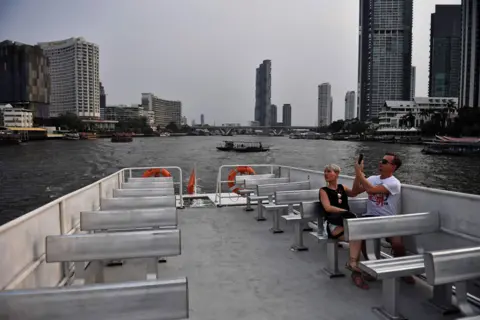 LILLIAN SUWANRUMPHA / AFP A lone couple take a tourist boat on the Chao Phraya River in Bangkok. 16 March