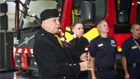 Dominic Salter FBU piper performs recital at ceremony in front of fire engine