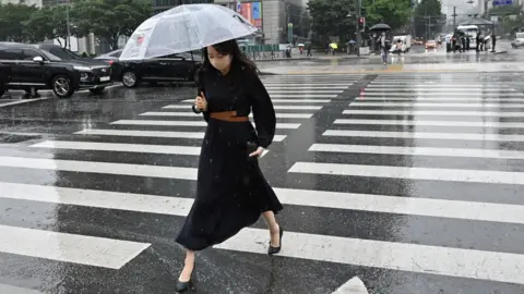 Getty Images A woman holding an umbrella crosses a road in central Seoul, South Korea.