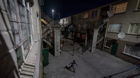 BBC/Shiraaz Mohamed A boy running between apartments in Manenberg, Cape Town - South Africa