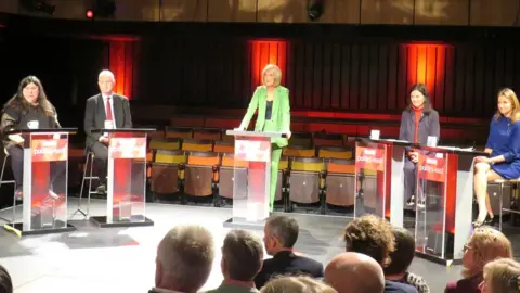 Nic Rigby/BBC The debate at the Perse School's Peter Hall Performing Arts Centre in Cambridge. Left to right: Naomi Bennett, leader of the Green Party on Cambridge City Council, Daniel Zeichner, Labour MP for Cambridge, BBC Politics East's Amelia Reynold, Bridget Smith, the Lib Dem leader of South Cambridgeshire District Council, and Lucy Frazer, the Conservative MP for South East Cambridgeshire