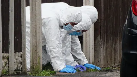 PA Media Forensic officers search the ground for evidence