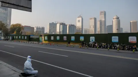 Reuters An epidemic prevention worker in a protective suit sits on the pavement in the Central Business District (CBD) as outbreaks of the coronavirus disease (COVID-19) continue in Beijing, November 23, 2022.