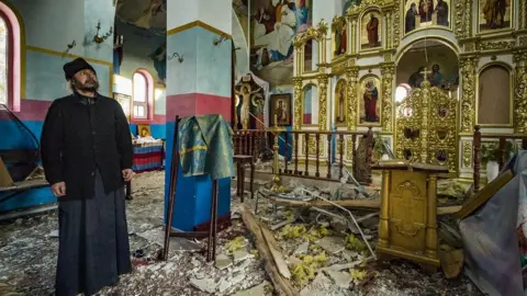 The priest of Yasnohorodka, stands inside his church destroyed because the combats between the Russian and Ukrainian armies