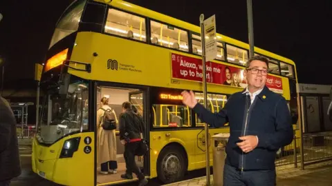 TFGM Andy Burnham by a Bee Network buses during the night