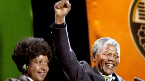 PA Nelson Mandela, with his then-wife Winnie, gives the famous clench-fist salute of the African National Congress to tens of thousands of fans who gathered to hear him at a concert in his honour at Wembley Stadium on 17 April 1990