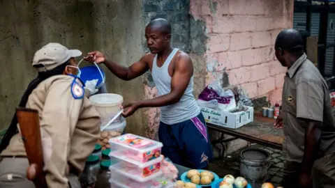 Getty Images A Gauteng Traffic Police officer confiscates goods from an informal trading post during a mixed patrol of South African National Defence Force (SANDF) and Gauteng Traffic Police in Alexandra, Johannesburg, on March 31, 2020. -