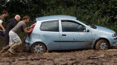 Getty Images Men pushing a car at a festival