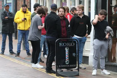 PA Media Men queue on the street to enter a Barbers