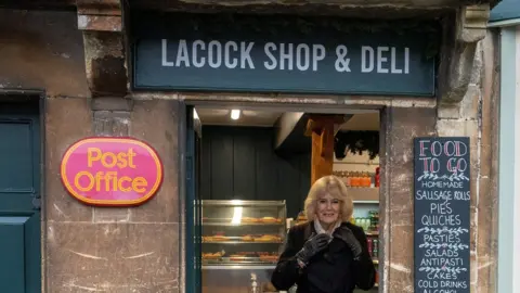 Reuters Camilla smiles in the doorway of Lacock Shop & Deli