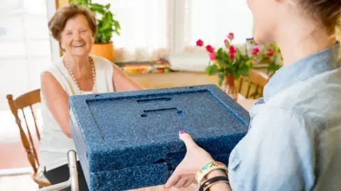 Getty Images An elderly woman getting a meals on wheel delivery