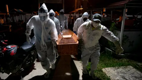 Getty Images Gravediggers wearing protective clothing carry the coffin of a victim of the coronavirus