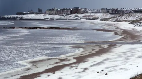 PA Beach covered in snow with buildings in the distance