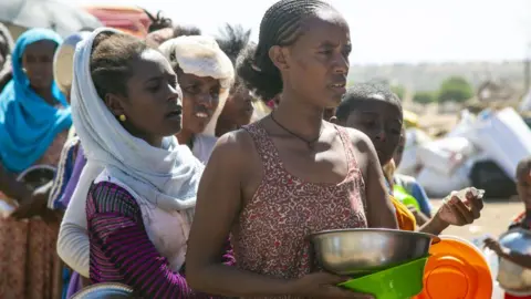 Getty Images Ethiopians, who fled the conflict in the Tigray region in northern Ethiopia due to the clashes in the operation launched by the Federal Government Forces against the Tigray People's Liberation Front (TPLF), wait to reiceve food in Hamdayit camp after reaching Kassala State, Sudan on December 14, 2020