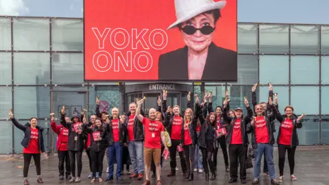 Lee Baxter MIF volunteers in front of a screen showing Yoko Ono