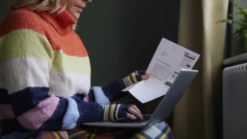 Woman In gloves with laptop and bill next to a radiator
