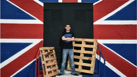 Charles McQuillan A man standing next to a union flag mural