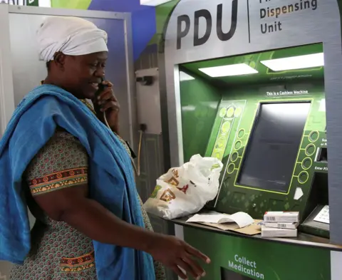 Reuters Rebecca Palai speaks on the phone with a consultant as she withdraws her medication at an ATM pharmacy which allows patients with chronic illnesses to receive repeat medication within three minutes, in Alexander township, South Africa, March 15, 2018.