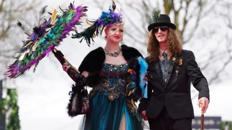 PA Media Woman holding parasol and man wearing a hat at Aintree Ladies Day 2024