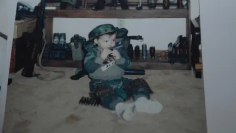 Handout via Getty images A photograph of a toddler sitting surrounded with weapons