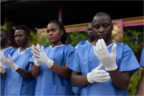 Getty Images Three people wearing medical scrubs and putting white gloves on.