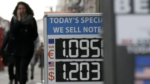 Getty Images A woman walks past a board displaying the price of Euro and US dollars against British pound