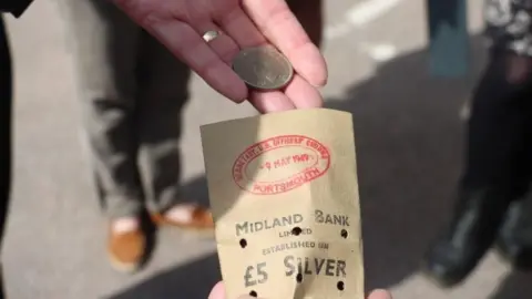 University of Portsmouth a small brown bag and a hand holding a silver coin