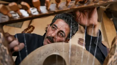 Fadel Dawod/ Getty Images Mohamed Ghaly, 56 years old, a simsimiya maker in Port Said on May 15, 2023. It is the Pharaonic instrument of the kanara, and it was very similar to the current harp instrument, except that it is smaller in size and has seven strings made of animal intestines.