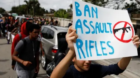 Reuters A young protester carries a sign reading "ban assault rifles"