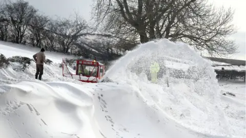 PA A homeowner watches over a snowblower as it clears the road which leads to the hamlet of Parkhead near Kirkoswald, Cumbria