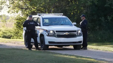 Getty Images Royal Canadian Mounted Police officers stand next to a police vehicle outside the house where one of the stabbing victims was found in Weldon, Saskatchewan, Canada, on September 6, 2022