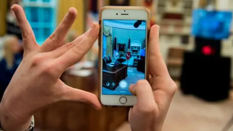 Getty Images Mr Trump - seen through a phone - speaks from the Oval Office at the White House