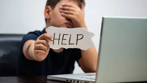 Getty Images Boy holds up help sign next to computer