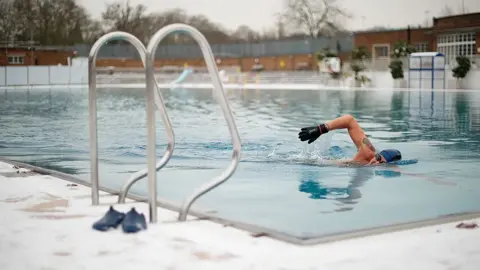 LEON NEAL/AFP via Getty Images Man swims in the lido in snowy weather