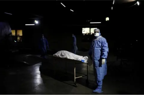 Reuters A health worker wearing personal protective equipment (PPE) stands next to the body of a man, who died from the coronavirus disease (COVID-19), before his cremation, at a crematorium in New Delhi, India April 21, 2021.