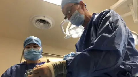 BBC News Surgeon Serryth Colbert performs a dental extraction in an operating theatre