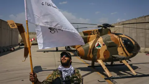 Getty Images A Taliban fighter raises a flag on the military airbase side of the Hamid Karzai International Airport