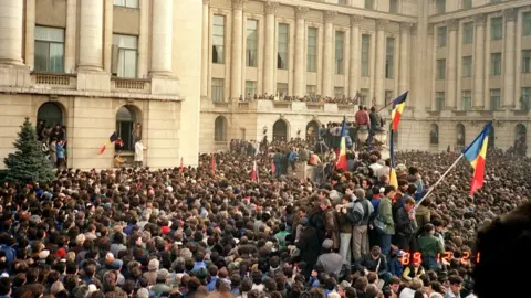 Getty Images Protesters in Bucharest wave Romanian flags as they stage an anti-communist demonstration at Republic Square, 21 December 1989