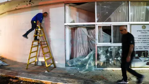 Reuters A man walks past a building in the northern Israeli town of Shlomi that was damaged by rockets fired from Lebanon (6 April 2023)