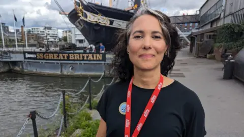 Iona Keen facing the camera, with the SS Great Britain behind her.