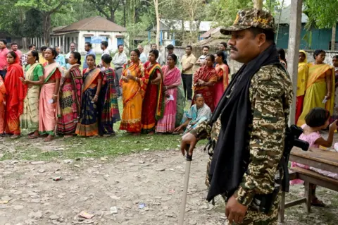 AFP A security personnel stands guard beside people in a queue waiting to cast their votes as voting starts in the first phase of India's general election at a polling station in Kalamati village, Dinhata distict of Cooch Behar in the country's West Bengal state on April 19, 2024