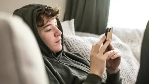 Getty Images Stock image of a teenager sitting on the sofa looking at their phone