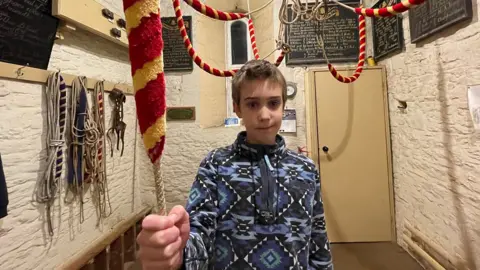 Boy smiles while holding bell-ringing cord