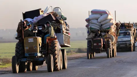 AFP Displaced Syrians travel along a road near the rebel-held town of Saraqeb in Idlib province (7 January 2018)