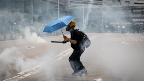 Getty Images A lone protester wearing a gas mask and carrying an umbrella surrounded by tear gas in Hong Kong