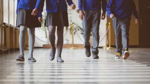 Getty Images Cropped image of school kids in uniform walking together in a row through corridor